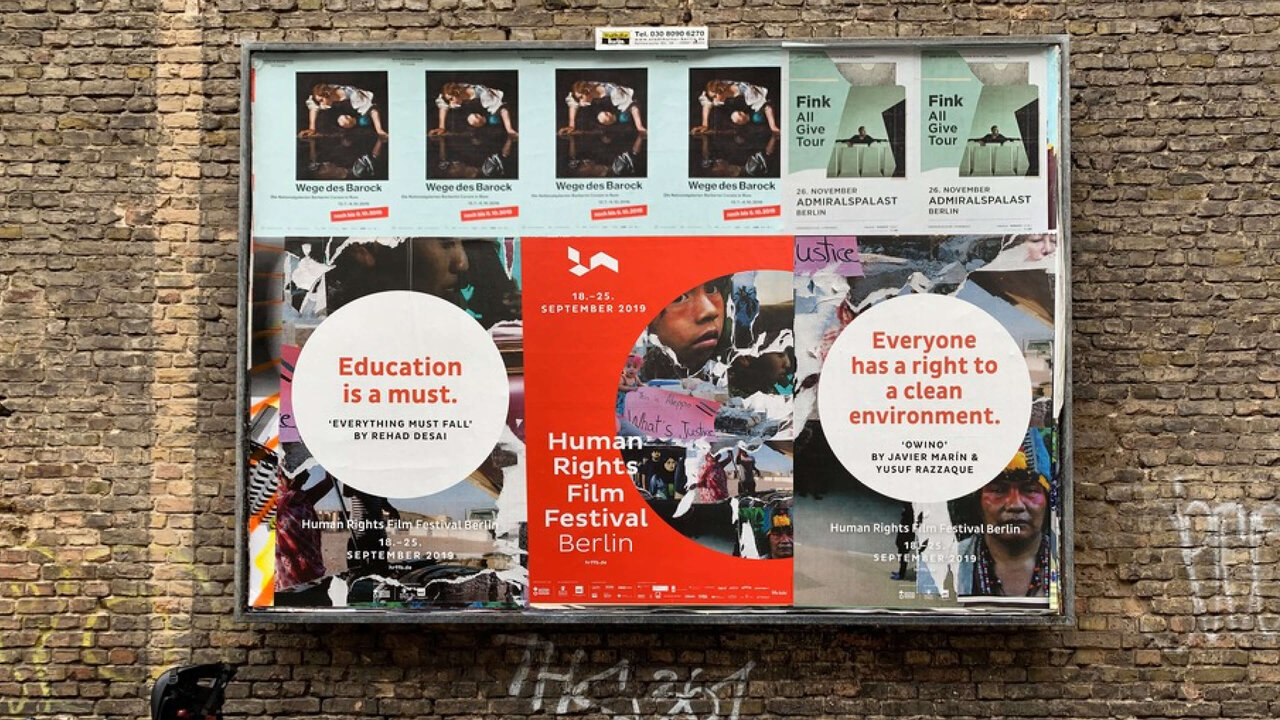Ein Plakat f&uuml;r das Human Rights Film Festival Berlin an einer Ziegelwand, mit wei&szlig;en und roten Informationsfeldern, die Aussagen &uuml;ber Bildung und Umweltrechte tragen. Verschiedene Filmplakate und Informationsmaterialien sind collageartig angeordnet.