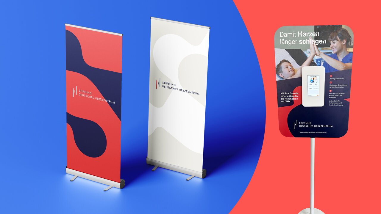 Zwei Roll-up-Banner und ein Poster-Display der Stiftung Deutsches Herzzentrum, gestaltet mit abstrakten Formen in Rot, Dunkelblau und Wei&szlig; sowie einem Foto-Motiv zum Thema Herzgesundheit.